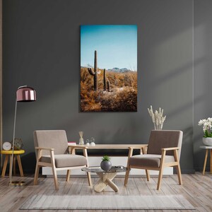May include: A living room interior with two brown armchairs, a coffee table, and a floor lamp. A framed print of a desert landscape with tall cacti hangs on the wall.