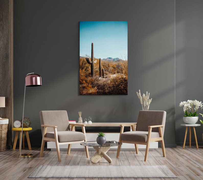 May include: A living room interior with two brown armchairs, a coffee table, and a floor lamp. A framed print of a desert landscape with tall cacti hangs on the wall.