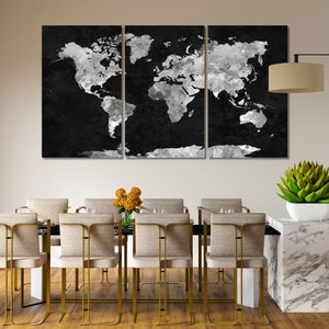 May include: A black and white world map canvas print in a three-piece set, hanging above a dining table with gold chairs and a white marble countertop.