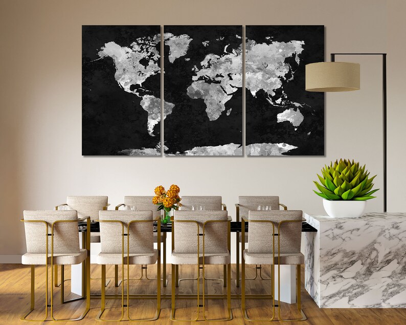 May include: A black and white world map canvas print in a three-piece set, hanging above a dining table with gold chairs and a white marble countertop.