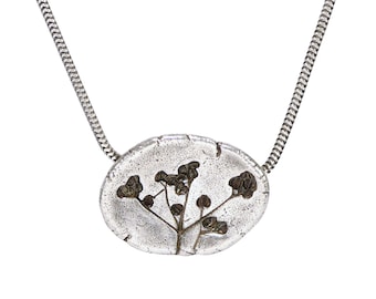 Puede incluir: Un collar de cadena de plata con un colgante ovalado de plata con una flor seca prensada.