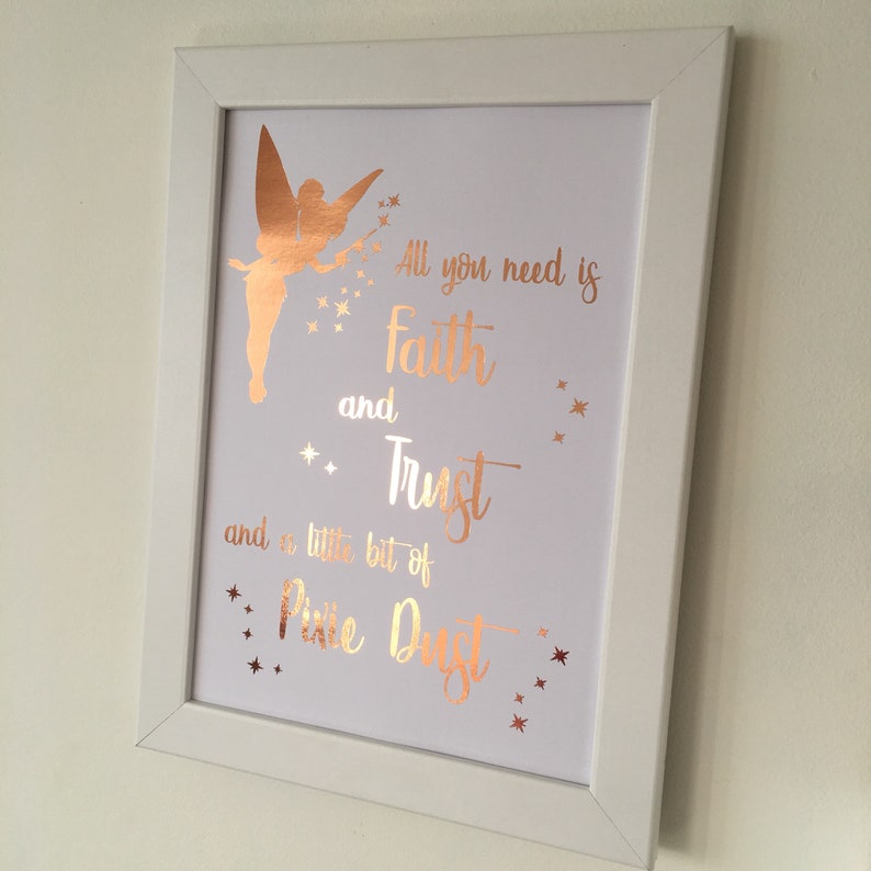 May include: A white framed print with a gold foil Tinkerbell silhouette and the quote "All you need is faith and trust and a little bit of pixie dust".