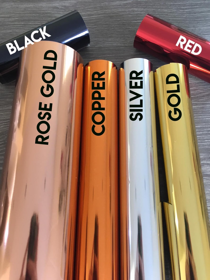 May include: Close-up of six rolls of metallic vinyl adhesive film in various colors: black, rose gold, copper, silver, gold, and red. The rolls are arranged horizontally, with the labels facing the viewer.
