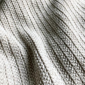 May include: Close-up of a soft, white crocheted blanket with a textured, ribbed pattern.