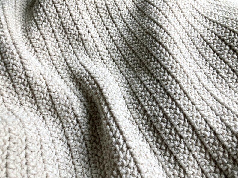 May include: Close-up of a soft, white crocheted blanket with a textured, ribbed pattern.