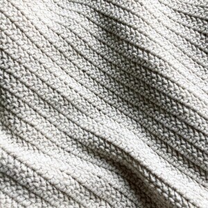 May include: Close-up of a textured, off-white fabric with a ribbed pattern. The fabric is soft and has a slightly grainy texture.