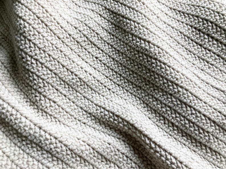 May include: Close-up of a textured, off-white fabric with a ribbed pattern. The fabric is soft and has a slightly grainy texture.