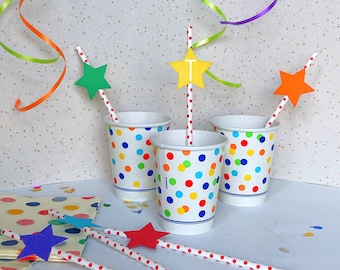Puede incluir: Tres vasos de papel blancos con lunares de colores, cada uno con una pajita y una tapa en forma de estrella. También se ven pajitas adicionales con tapas de estrella y una servilleta de lunares. Serpentinas de fiesta de varios colores en el fondo.