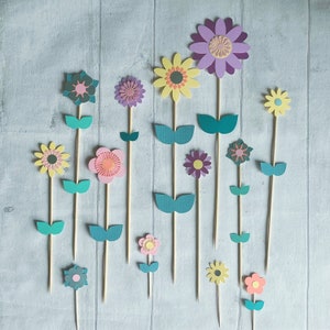 Pu&ograve; includere: Un set di 14 topper di fiori di carta in vari colori, tra cui viola, rosa, giallo e verde. I fiori sono attaccati a spiedini di legno e hanno una variet&agrave; di disegni, tra cui cerchi semplici, stelle e motivi floreali pi&ugrave; complessi.