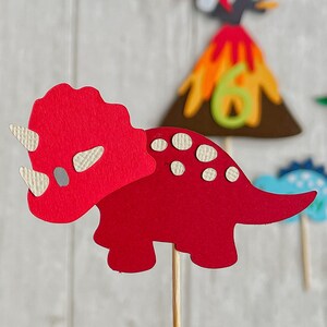 May include: Red paper dinosaur with white spots, a red and white horn, and a wooden stick for a stand. The dinosaur is a triceratops.