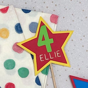 May include: A red star-shaped cake topper with a yellow border and a green number 4. The name "ELLIE" is written in white on the star.