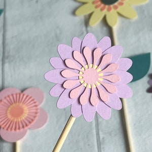 Pu&ograve; includere: Un set di tre topper di fiori di carta in tonalit&agrave; rosa, giallo e viola. I fiori sono sovrapposti e hanno un aspetto delicato e fantasioso. Sarebbero perfetti per aggiungere un tocco primaverile a una torta o ad un altro progetto artigianale.