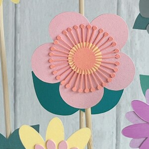 Pu&ograve; includere: Un fiore di carta rosa con un centro giallo e arancione. Il fiore &egrave; attaccato a un bastoncino di legno e ha foglie verdi.