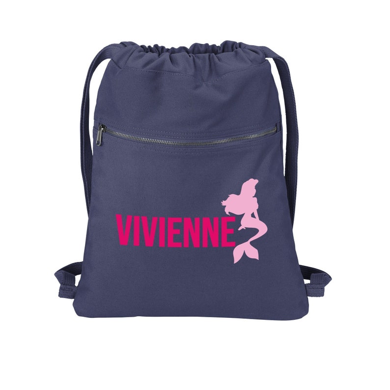 Puede incluir: Una mochila azul marino con cord&oacute;n de ajuste, un bolsillo con cremallera y una silueta de sirena rosa con el nombre "VIVIENNE" impreso en rosa.