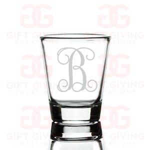 May include: A clear glass shot glass with a silver monogram of the letter "B" in a decorative script font.