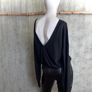 May include: Black long-sleeved shirt with a deep V-neck and a low back. The shirt is paired with black leather pants.