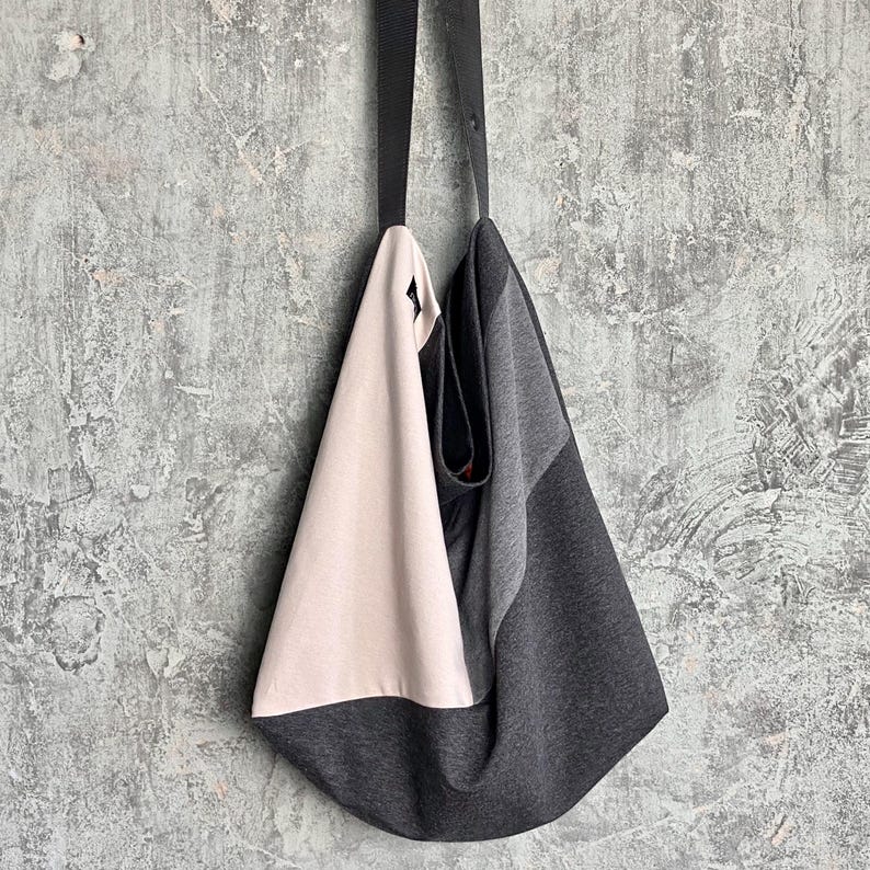 May include: A grey and beige tote bag with a black strap. The bag is made of a soft, textured fabric.