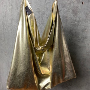 Pode incluir: Uma bolsa tote met&aacute;lica dourada com um design descontra&iacute;do e sem estrutura. A bolsa tem um estilo simples e minimalista e &eacute; feita de um material macio e flex&iacute;vel.
