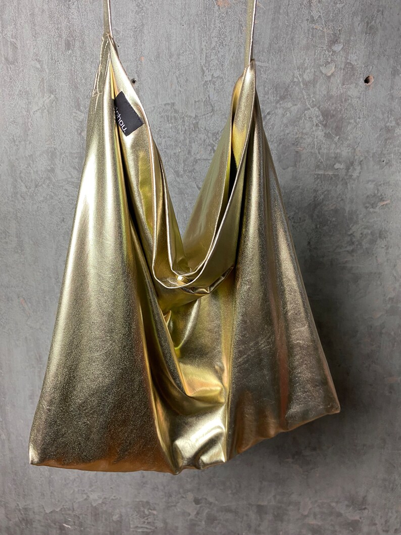 Pode incluir: Uma bolsa tote met&aacute;lica dourada com um design descontra&iacute;do e sem estrutura. A bolsa tem um estilo simples e minimalista e &eacute; feita de um material macio e flex&iacute;vel.
