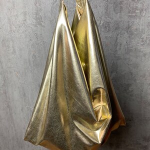Pode incluir: Uma bolsa tote dourada met&aacute;lica com um design descontra&iacute;do e sem estrutura. A bolsa tem duas al&ccedil;as e &eacute; feita de um material brilhante e liso.