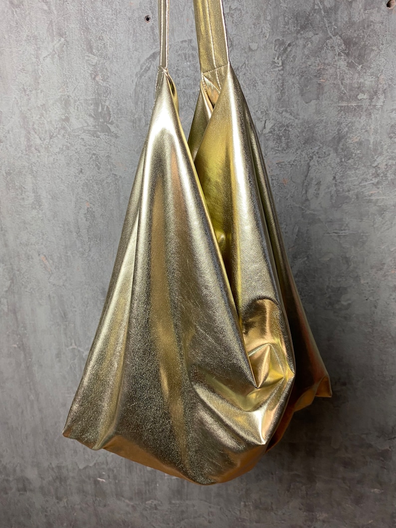 Pode incluir: Uma bolsa tote dourada met&aacute;lica com um design descontra&iacute;do e sem estrutura. A bolsa tem duas al&ccedil;as e &eacute; feita de um material brilhante e liso.