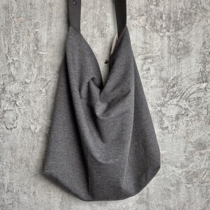 May include: A grey slouchy tote bag with black straps. The bag is made of a soft, textured fabric.