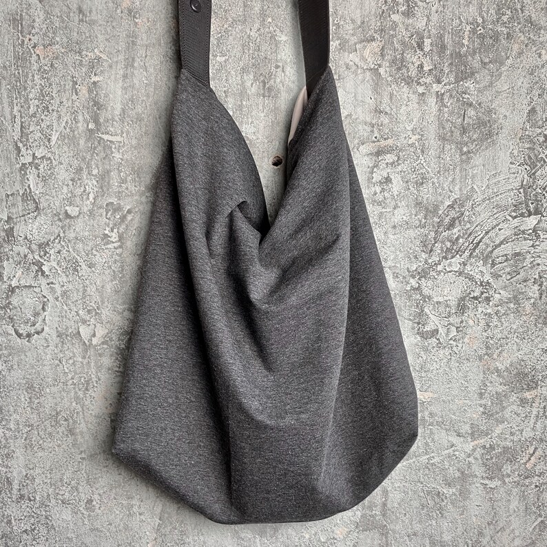 May include: A grey slouchy tote bag with black straps. The bag is made of a soft, textured fabric.