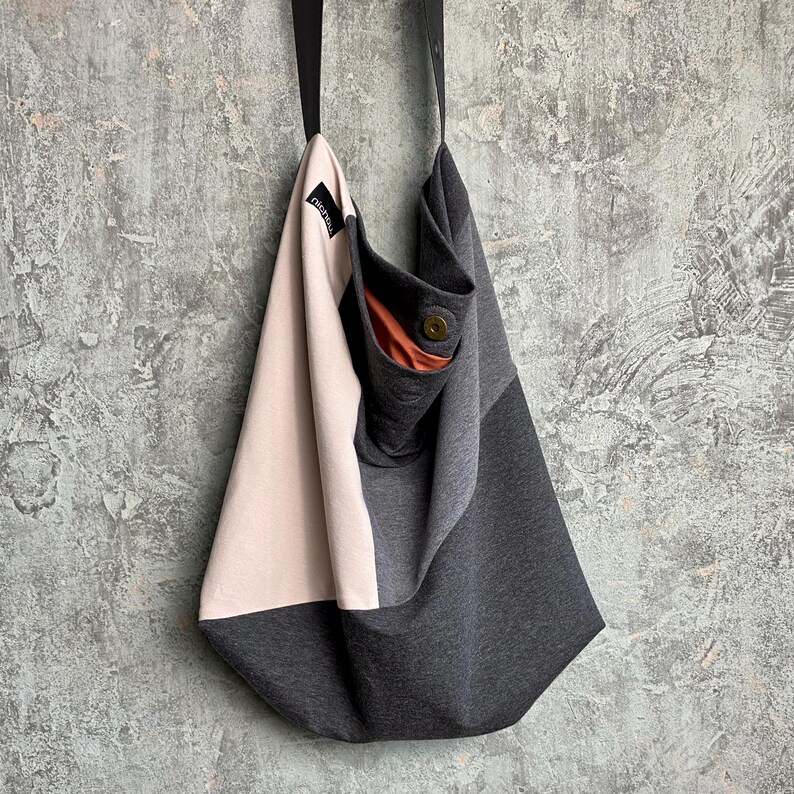 May include: A grey and pink fabric tote bag with a small brown pocket. The bag has a long strap and is made of a soft, comfortable material.