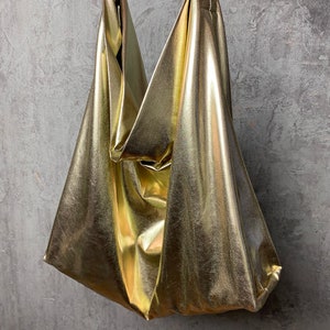 Pode incluir: Uma bolsa tote met&aacute;lica dourada com um design descontra&iacute;do e sem estrutura. A bolsa tem uma al&ccedil;a &uacute;nica e &eacute; feita de um material macio e flex&iacute;vel.