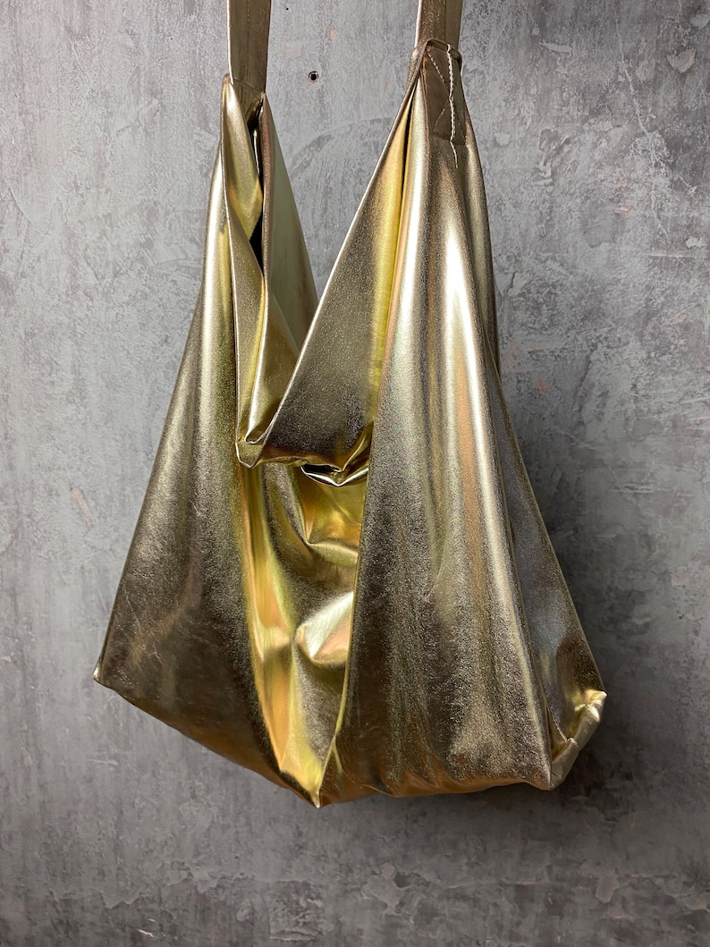 Pode incluir: Uma bolsa tote met&aacute;lica dourada com um design descontra&iacute;do e sem estrutura. A bolsa tem uma al&ccedil;a &uacute;nica e &eacute; feita de um material macio e flex&iacute;vel.