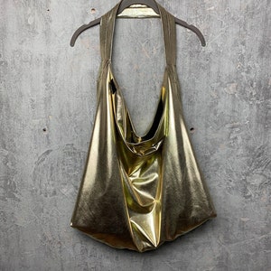 Pode incluir: Uma bolsa tote dourada met&aacute;lica pendurada em um galho de madeira. A bolsa &eacute; feita de um material macio e brilhante e tem um visual casual e descontra&iacute;do.