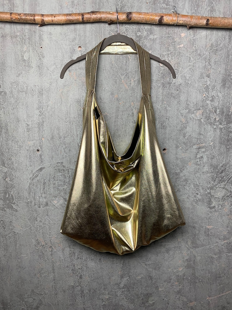 Pode incluir: Uma bolsa tote dourada met&aacute;lica pendurada em um galho de madeira. A bolsa &eacute; feita de um material macio e brilhante e tem um visual casual e descontra&iacute;do.