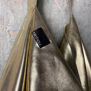 Pode incluir: Uma bolsa de tecido met&aacute;lico dourado com uma etiqueta preta que diz "nichou".