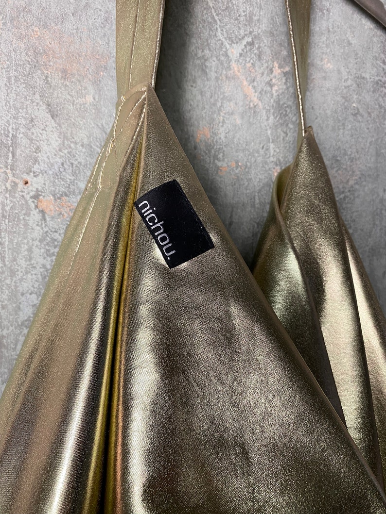 Pode incluir: Uma bolsa de tecido met&aacute;lico dourado com uma etiqueta preta que diz "nichou".