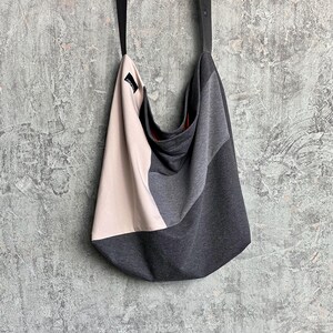 May include: A grey, beige and black fabric tote bag with a black strap. The bag has a slouchy, casual design.