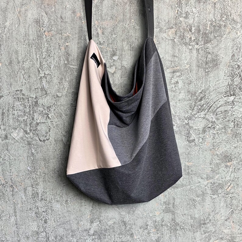 May include: A grey, beige and black fabric tote bag with a black strap. The bag has a slouchy, casual design.