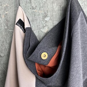 May include: A grey and pink fabric tote bag with a brown fabric lining. The bag has a black label with the word "nichou" on it. The bag has a gold metal snap closure.
