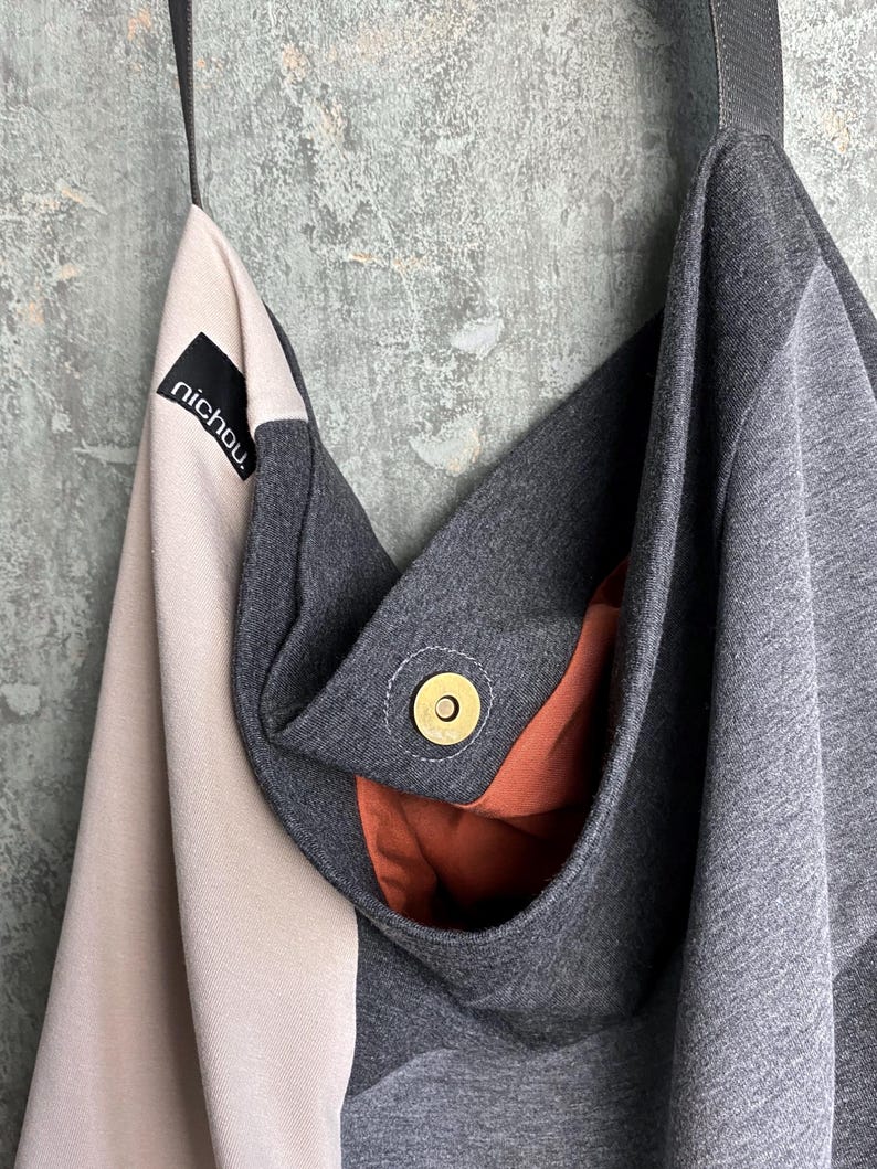 May include: A grey and pink fabric tote bag with a brown fabric lining. The bag has a black label with the word "nichou" on it. The bag has a gold metal snap closure.