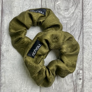 Könnte beinhalten: Zwei grüne Scrunchies mit Paisley-Muster und schwarzen Etiketten mit der Aufschrift "nichou."