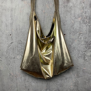 Pode incluir: Uma bolsa tote met&aacute;lica dourada com um design descontra&iacute;do e sem estrutura. A bolsa tem uma abertura larga e duas al&ccedil;as longas.