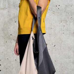 May include: A large, grey and beige tote bag with a black strap. The bag is made of a soft, fabric material and has a simple, modern design.