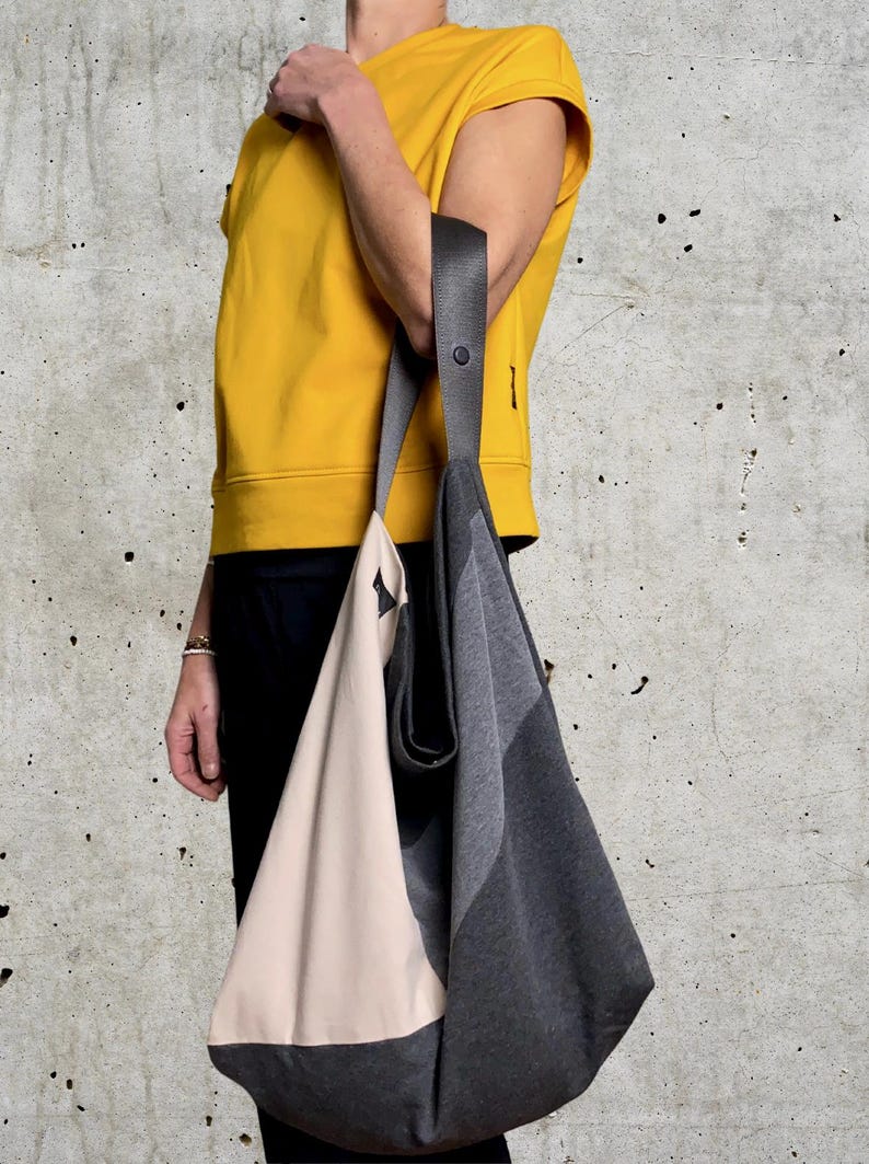 May include: A large, grey and beige tote bag with a black strap. The bag is made of a soft, fabric material and has a simple, modern design.