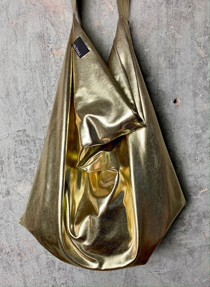 Pode incluir: Uma bolsa tote dourada met&aacute;lica com uma etiqueta preta que diz "nichou".