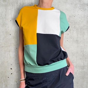 Könnte beinhalten: Ein kurzärmeliges Shirt mit geometrischem Muster in Gelb, Weiß, Schwarz und Grün.