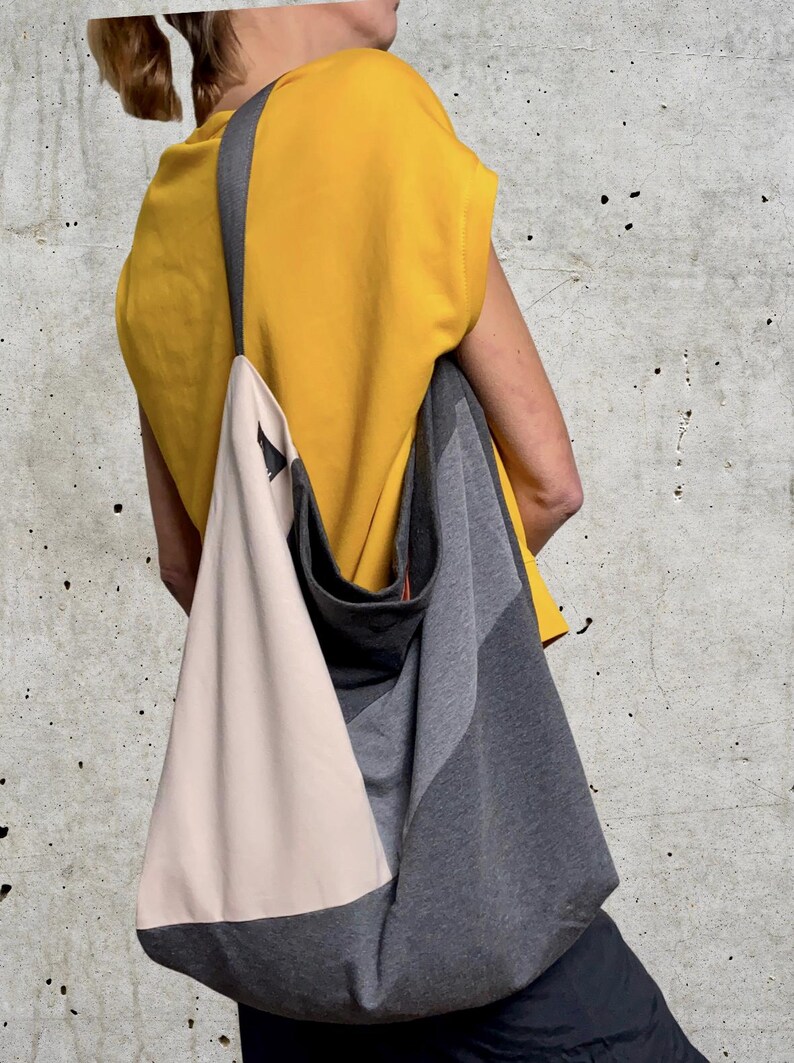 May include: A person wearing a yellow top and black trousers is carrying a large, grey and beige tote bag with a black strap.