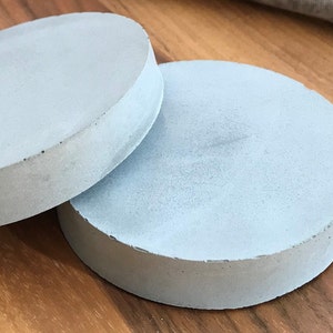 Könnte beinhalten: Zwei runde Untersetzer aus hellem Beton. Die Untersetzer sind glatt und haben eine leicht strukturierte Oberfläche.
