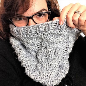 Könnte beinhalten: Ein silbergrauer gestrickter Schal mit einem Zopfmuster.