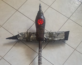 Op de afbeelding: Een handgemaakte, donkere houten staf met een decoratieve top met een rood, gloeiend ontwerp. De staf heeft een gewikkelde handgreep en een kruis en rozenkrans bevestigd. De staf is ongeveer 152 cm lang.