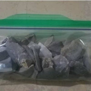 May include: A clear plastic bag with a green zipper closure contains a collection of gray, irregularly shaped rocks.