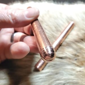 May include: Two copper-colored metal rods with rounded ends. The rods have a textured surface and are held in a hand.